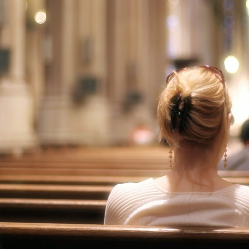 Blonde woman sitting on a church bench praying