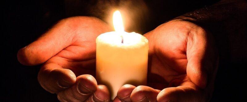 Hands holding a lit candle in darkness