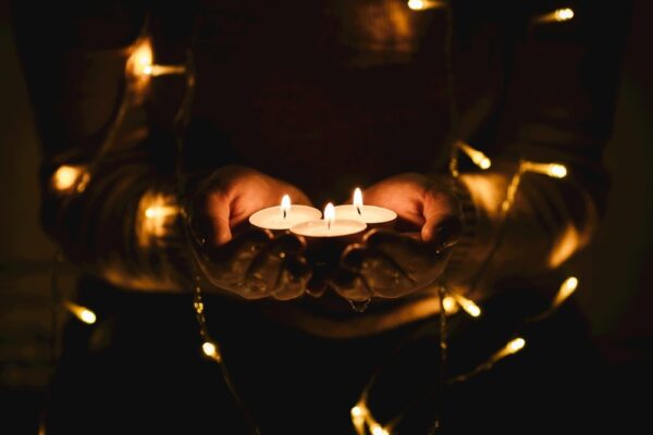 hands in the darkness holding tea lights with fairy lights wrapped around their arms